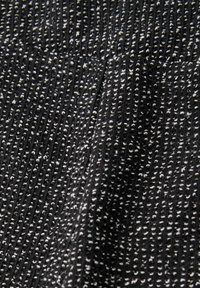 Czarna tkanina o fakturze prążkowanej z drobnymi białymi plamkami na całej powierzchni. Materiał wydaje się miękki i lekko rozciągliwy.