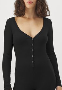 Bodysuit noir à manches longues côtelé, avec un décolleté en V profond et des fermetures à pression à l'avant, possédant une texture lisse et un design ajusté.