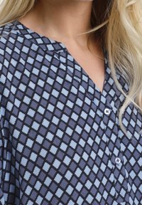 Luźna bluzka w granatowym kolorze z jasnoniebieskim geometrycznym wzorem w diamenty, z dekoltem w serek i zapięciem na guziki.