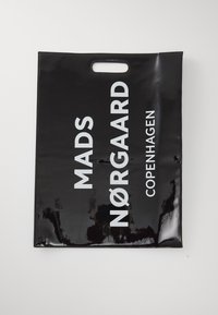 Schwarze, glänzende Plastiktüte mit einem Ausstanzauschnitt für die Hand. Mit auffälligem weißen Text: "MADS NØRGAARD KOPENHAGEN", der deutlich sichtbar ist.