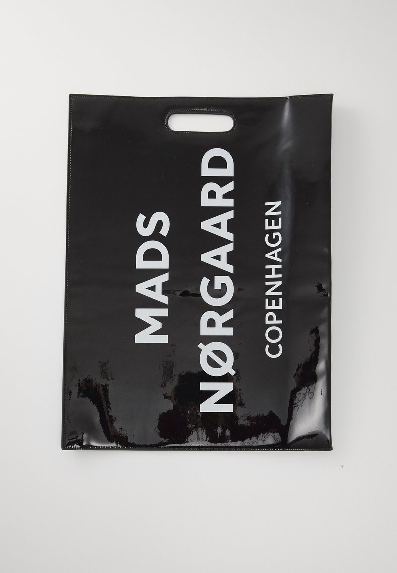 Bolsa de plástico negra y brillante con un asa recortada. Presenta un texto en blanco en negrita: "MADS NØRGAARD COPENHAGUE" claramente visible.