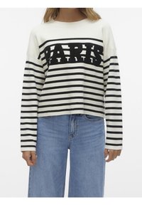 Pull à rayures blanches et noires avec un design court, arborant le lettrage audacieux "PARIS" sur la poitrine, associé à un jean taille haute bleu.