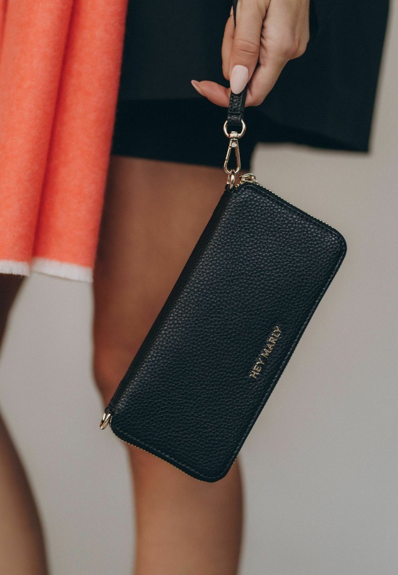 Zwarte gekorrelde leren portemonnee met een ritsluiting, gouden hardware en een polsband. Merknnaam in reliëf op de voorkant.