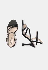Sandalias de tacón alto negras con múltiples correas delgadas, punta abierta y hebilla en el tobillo. Textura de cuero suave y un tacón de aguja esbelto.