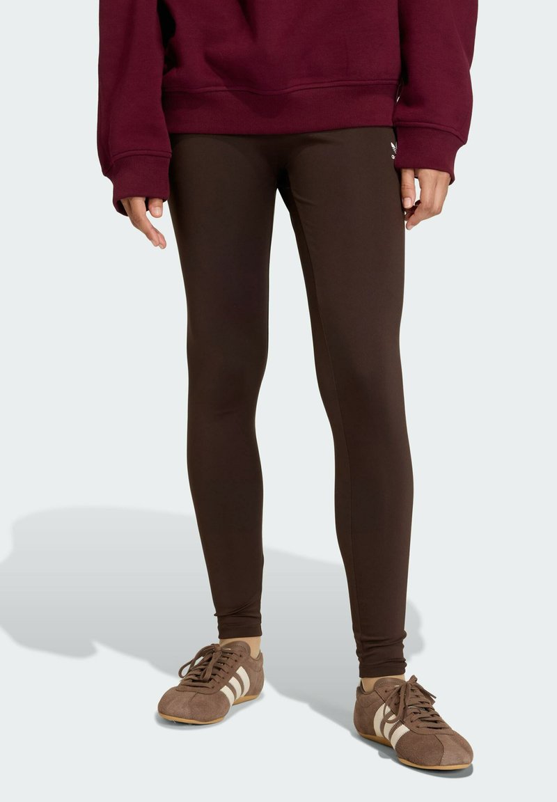 Leggings marroni realizzati in materiale elastico, con una consistenza liscia e un design aderente, abbinati a scarpe sportive marroni scure.