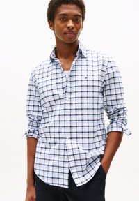 Chemise à carreaux bleu clair en coton avec un col boutonné, ornée d'accents navy et bleu foncé. Manches retroussées.