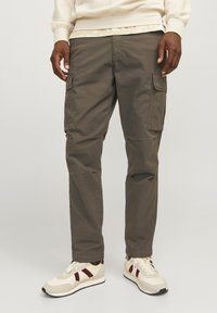 Pantaloni cargo din bumbac verde măsliniu, cu buzunare laterale, picioare conice și cusături întărite. Asortați cu adidași bej cu accente roșii.