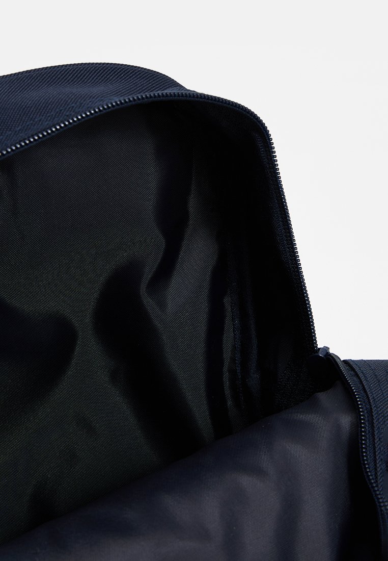 Borsa blu navy con zip, dotata di un esterno liscio e un rivestimento testurizzato. L'interno presenta un unico scomparto con una superficie morbida e opaca.