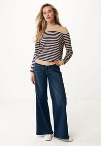 Pull rayé en beige et marine, avec un col haut et des boutons aux épaules, associé à un jean en denim bleu à jambes larges.