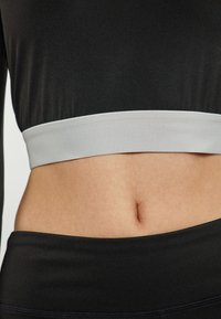Zwarte cropped top met een grijze elastische band, met een gladde textuur en een aansluitend ontwerp, gecombineerd met hoge zwarte onderkleding.