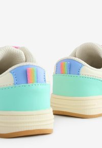 Des baskets colorées avec une base vert menthe, des accents bleus et un talon texturé. Elles présentent une languette à rayures multicolores et une semelle de couleur crème.
