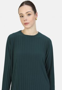 Tumman vihreä ribbikappale, jossa on pitkät hihat, pyöreä kaulus ja sileä pinta. Ominaisuuksiin kuuluu minimalistinen muotoilu ilman kuvioita tai lisäkoristeita.