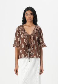 Blusa marrone a fantasia con maniche a volant, scollo a V profondo e chiusura con cravatta davanti. Presenta motivi a foglia in crema su uno sfondo testurizzato.