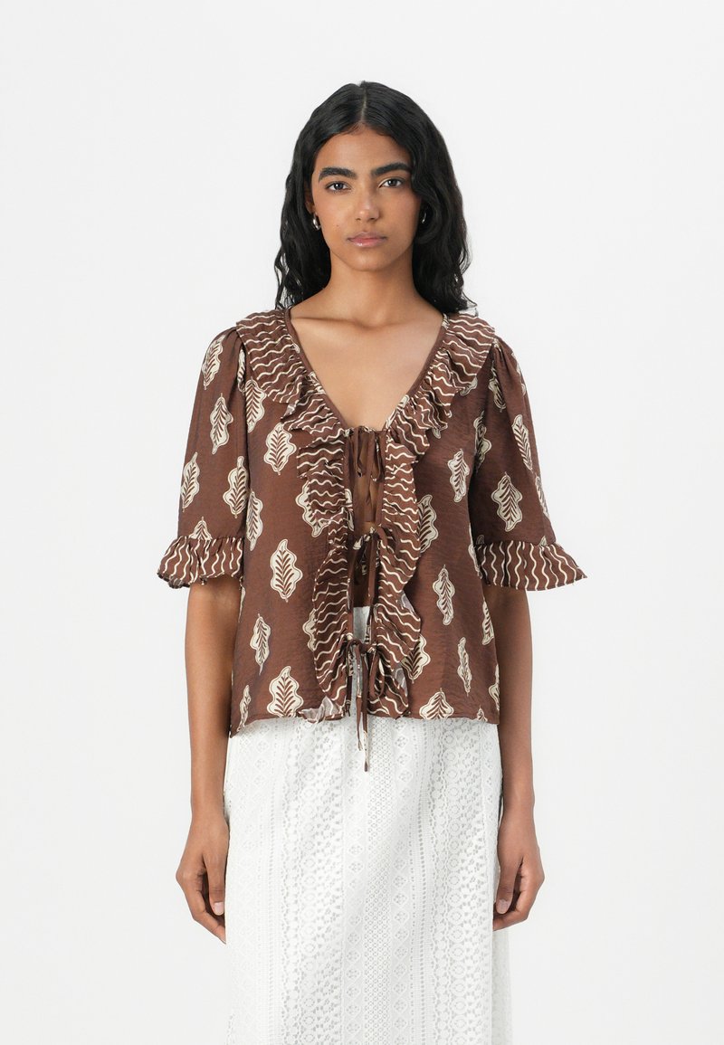 Blusa marrone a fantasia con maniche a volant, scollo a V profondo e chiusura con cravatta davanti. Presenta motivi a foglia in crema su uno sfondo testurizzato.