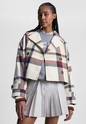 Cropped plaid jacket in cream, red, and navy with large lapels and double-breasted buttons; paired with a light gray sweater and pleated skirt.
