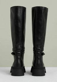 Svarta läderstövlar knähöga med tjocka sulor, utrustade med två remmar med spännen för justerbar passform. Slät yta och minimalistisk design.