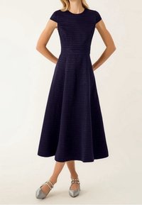 Marinblå, knälång A-linjeformad klänning med korta ärmar, ribbad textur, åtsittande liv och en utsvängd kjol, kombinerad med silverfärgade flats.
