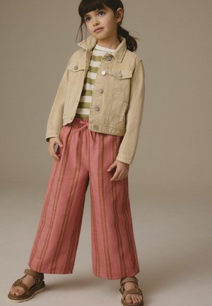 Veste en denim beige clair sur une chemise rayée verte et blanche ; associée à un pantalon large rayé rose. Des sandales marron complètent la tenue.