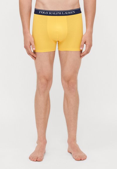 Rumene bokserice z oprijeto prileganje, z temno modrim pasom z oznako "POLO RALPH LAUREN." Mehka, gladka tkanina brez vzorcev.