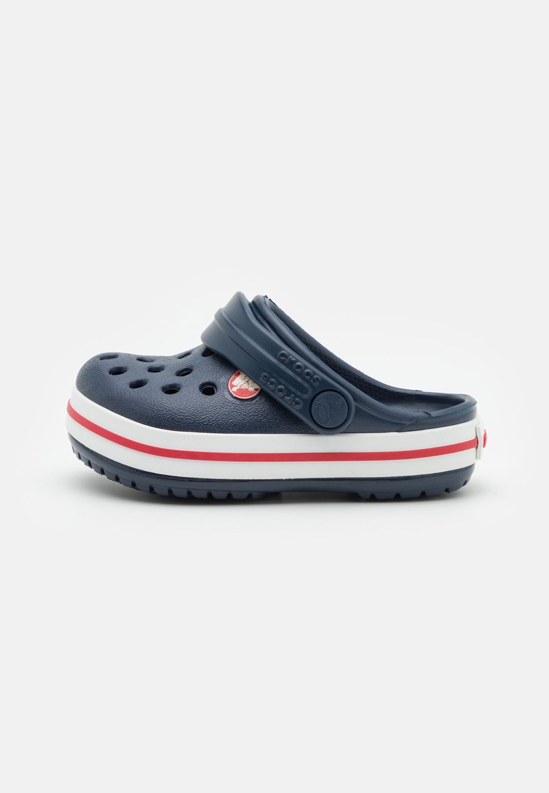 Sabot Crocs bleu marine avec des trous d'aération, une semelle rayée rouge et blanc, et une bride de talon réglable sur fond blanc.