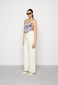 Top cropped estampado com design floral em roxo, branco e rosa; combinado com calças largas de cintura alta em creme e sapatos amarelos de slip-on.