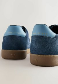 Plave nubuck tenisice s svijetlos plavim akcentima, s teksturiranom srednjom potplatom i otisnutim brandom na peti. Smeđi gumenji potplat.