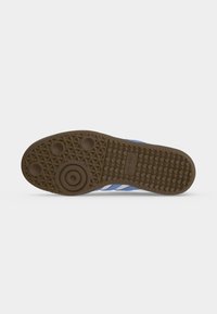 Semelle bleue de basket Adidas face vers le haut montrant une bande de roulement marron à motifs avec des formes d’adhérence circulaires et triangulaires ainsi que le logo Adidas.