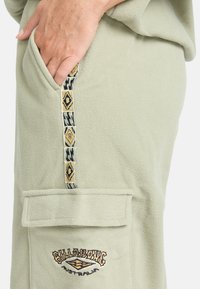 Lichtgroene fleece broeken met een grote voorkant zak, voorzien van een decoratieve gestreepte patroon langs de zijkant en geborduurd logo detail.