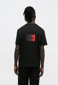 Μαύρο κοντομάνικο t-shirt με ορθογώνιο κόκκινο και μαύρο λογότυπο στην πλάτη, κατασκευασμένο από βαμβακερό ύφασμα, με άνετη εφαρμογή.