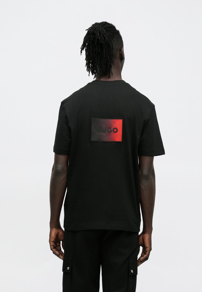 Μαύρο κοντομάνικο t-shirt με ορθογώνιο κόκκινο και μαύρο λογότυπο στην πλάτη, κατασκευασμένο από βαμβακερό ύφασμα, με άνετη εφαρμογή.