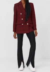 Rot kariertes, doppelt geknöpftes Blazer mit silbernen Knöpfen, kombiniert mit schwarzen, ausgestellten Hosen mit Schlitzen am Saum und weißen Sneakers.