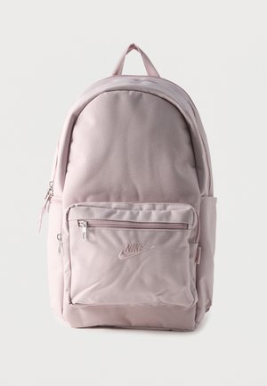 Mochila de tela rosa claro con bolsillo frontal con cremallera, bolsillo lateral, asa superior y logotipo de Nike bordado en el bolsillo frontal.