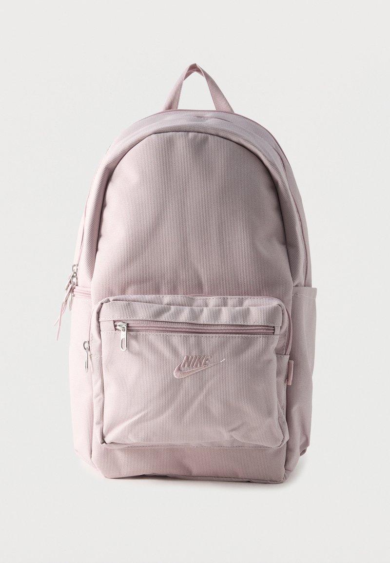 Svetloružový textilný batoh s predným vreckom na zips, bočným vreckom, horným uchom a vyšitým logom Nike na prednom vrecku.