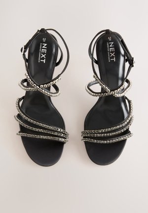 Sandali neri con tacco, dotati di molteplici cinturini argentati scintillanti, con superficie lucida e fibbia regolabile alla caviglia. Interno marchiato "NEXT".