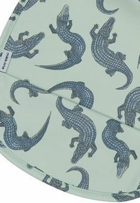 Vzorkovaná látka s jemne mätovým pozadím a viacerými modrými ilustráciami aligátorov. Hladká štruktúra s detailnými šupinami a akcentmi.