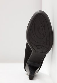 Chaussure à talons hauts en daim noir avec un bout pointu et une semelle en caoutchouc texturée présentant un motif subtil. Hauteur du talon d'environ sept centimètres.