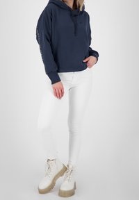 Sudadera azul marino con cordón, con mangas largas. Combinada con jeans ajustados blancos y botas de suela gruesa color crema.