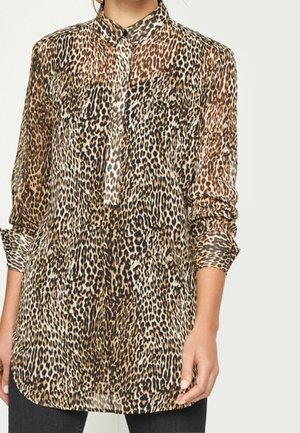 Blusa de manga larga con estampado de leopardo y botones, con cuello clásico, combinada con pantalones negros, usada por una persona contra un fondo liso.