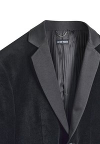 Chaqueta de traje de terciopelo negro con solapa de satén. El interior muestra un forro texturizado y a rayas. La etiqueta dice "ANTHONY MORATO."