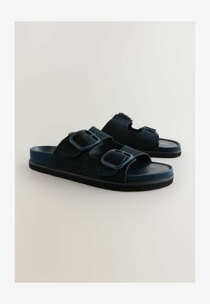 Tume sinine sametist libisemisjalanõud, millel on kaks reguleeritavat rihma, millel on ristkülikukujulised pandlad, ja lame kummist tõstepõhi. Sile sisekeel.