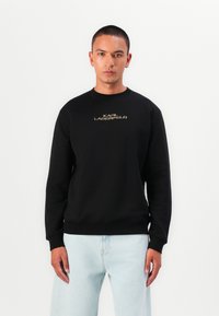 Sweatshirt preto feito de mistura de algodão, com gola redonda e punhos canelados. Texto dourado "KARL LAGERFELD" centrado no peito.