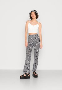 Top branco cropped com detalhe amarrado, calças largas pretas e brancas com padrão, e sandálias plataformas pretas e grossas. Acessorizado com um chapéu estilo balde.
