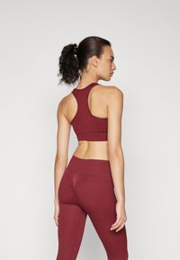 Top deportivo corto burdeos con diseño de espalda nadadora y leggins de cintura alta a juego, que presentan una textura canalé y una silueta ajustada.