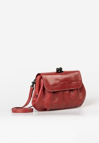 Red leather handbag with a rounded shape, magnetic snap closure, and a detachable strap. Smooth texture with subtle folding details.