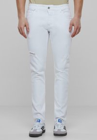 Jeans blancos de corte ajustado, con detalles desgastados en las rodillas; estilizados con cierre de botón y diseño de cinco bolsillos.