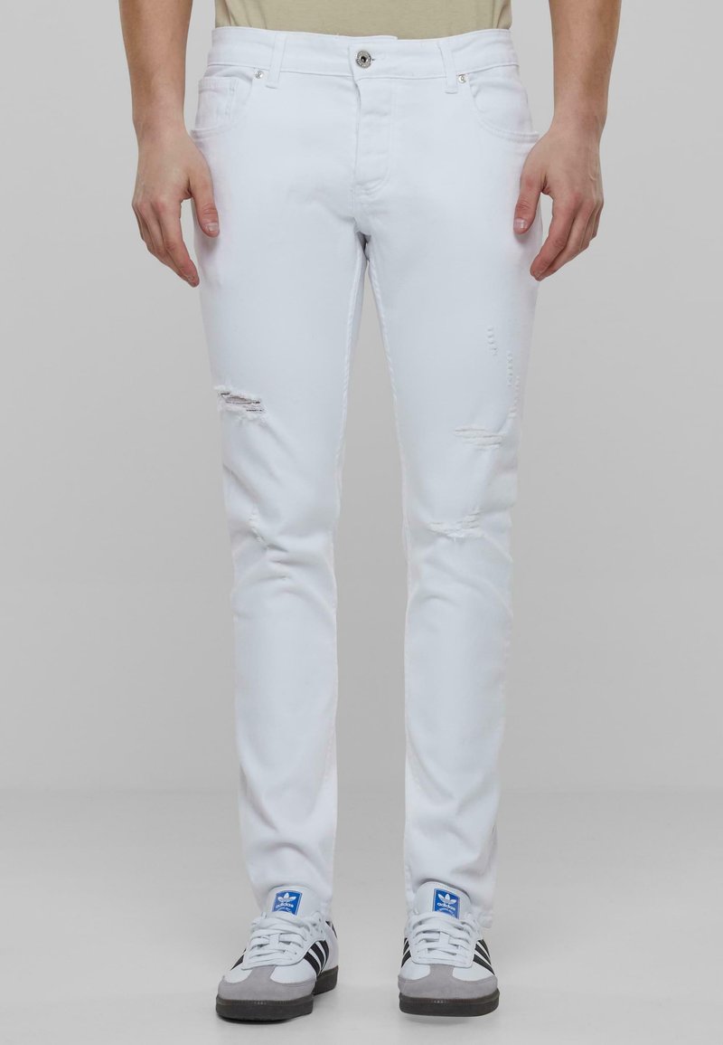 Fehér, slim fit farmernadrág, lelőtt részletekkel a térdnél; gombos záródással és öt zsebbel készült.