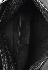 Interno di una borsa a tracolla in pelle nera con finitura testurizzata, fodera in tessuto, una tasca con zip e un'etichetta prominente.