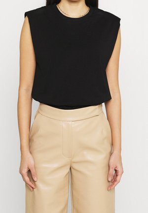 Top negro sin mangas con diseño de hombros anchos, hecho de un material suave. Combinado con pantalones de cuero beige de cintura alta.