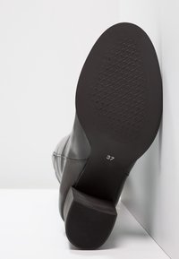 Bottine en cuir noir avec une semelle en caoutchouc texturée, un talon bloc épais, et la taille 37 indiquée sous la chaussure, présentant un design élégant.