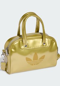 Metallic gold handbag with dual handles, zip closure, and detachable strap. Features embossed logo and shiny smooth surface.
